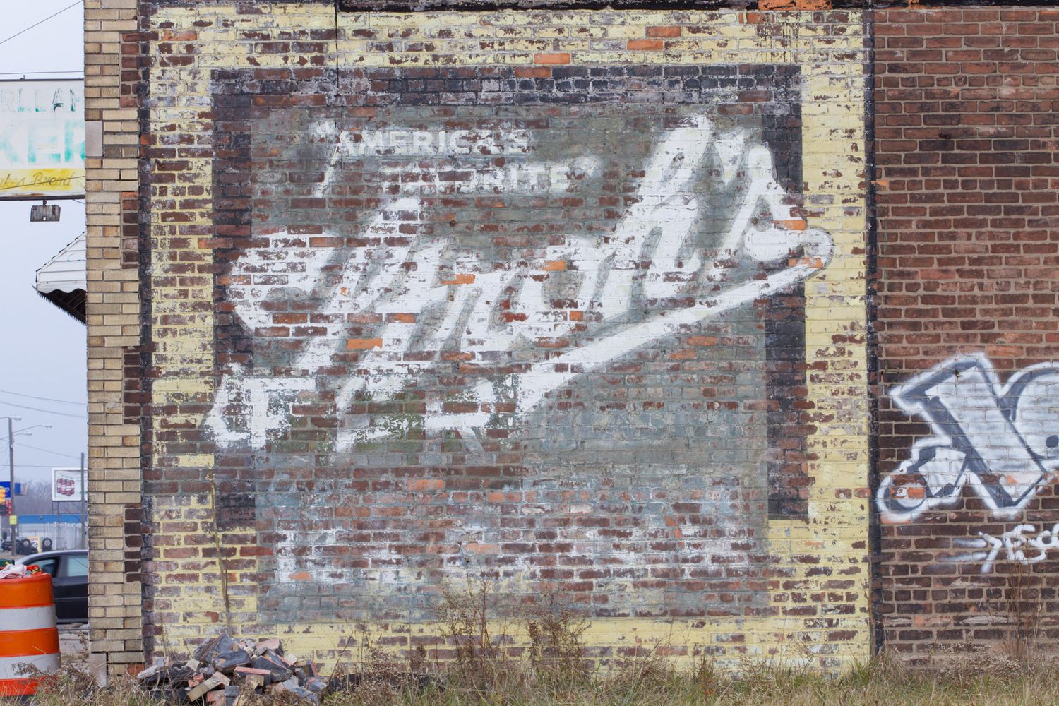 Faded ghost sign on a weathered brick wall reading America's favorite with vintage advertisement artwork and graffiti.