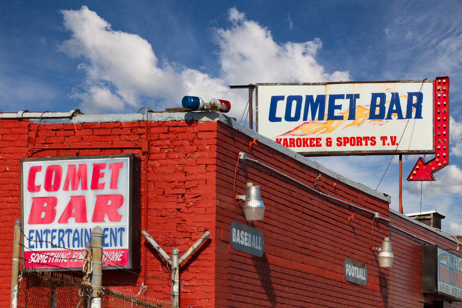 Comet Bar with karaoke and sports TV signage on a red brick building under a blue sky.