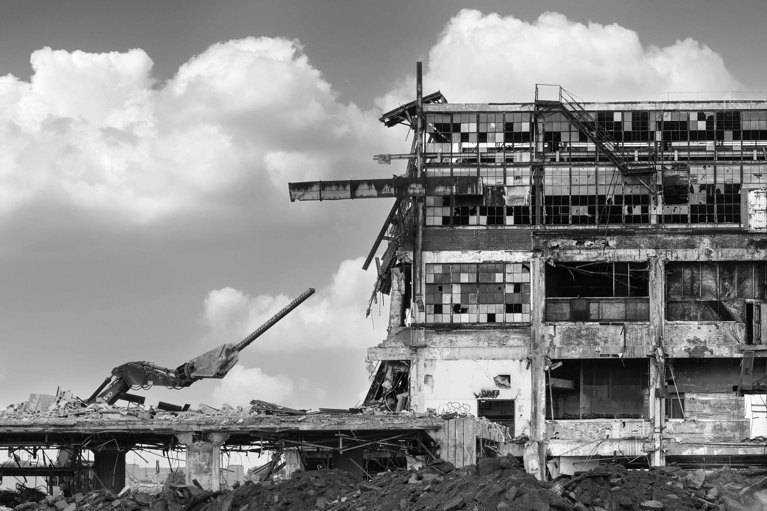 Black and white image of the abandoned Cadillac Stamping plant in Detroit with machinery holding a steel beam during demolition.
