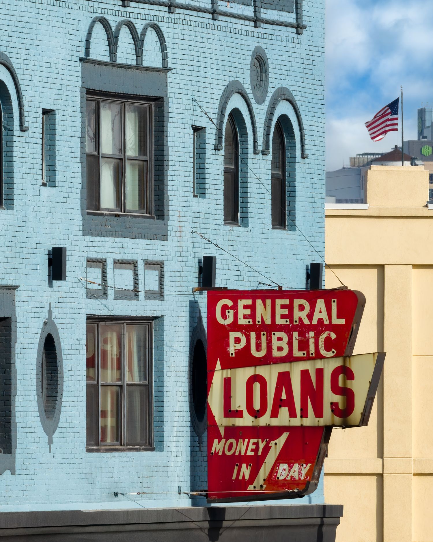 A red and yellow vintage sign advertising loans and money services on the side of a light blue building in Corktown Detroit Michigan.