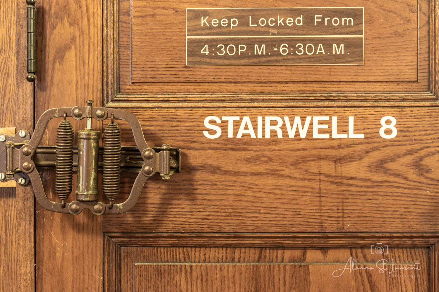 Wooden door with brass lock hardware labeled Stairwell 8, featuring a Keep Locked From 4:30PM-6:30AM sign.