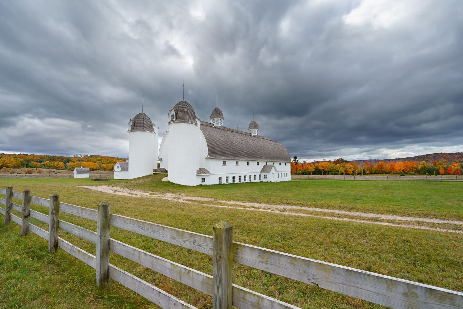 DH Day barn with wooden fence under dramatic stormy skies in rural landscape in the fall in Michigan.