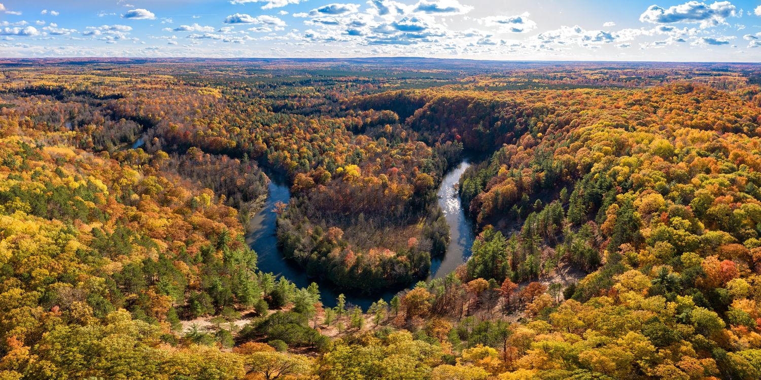 Aerial panorama of the Manistee river through vibrant autumn forest and blue skies at the High Rollway Scenic Overlook in Kingsley, MI.