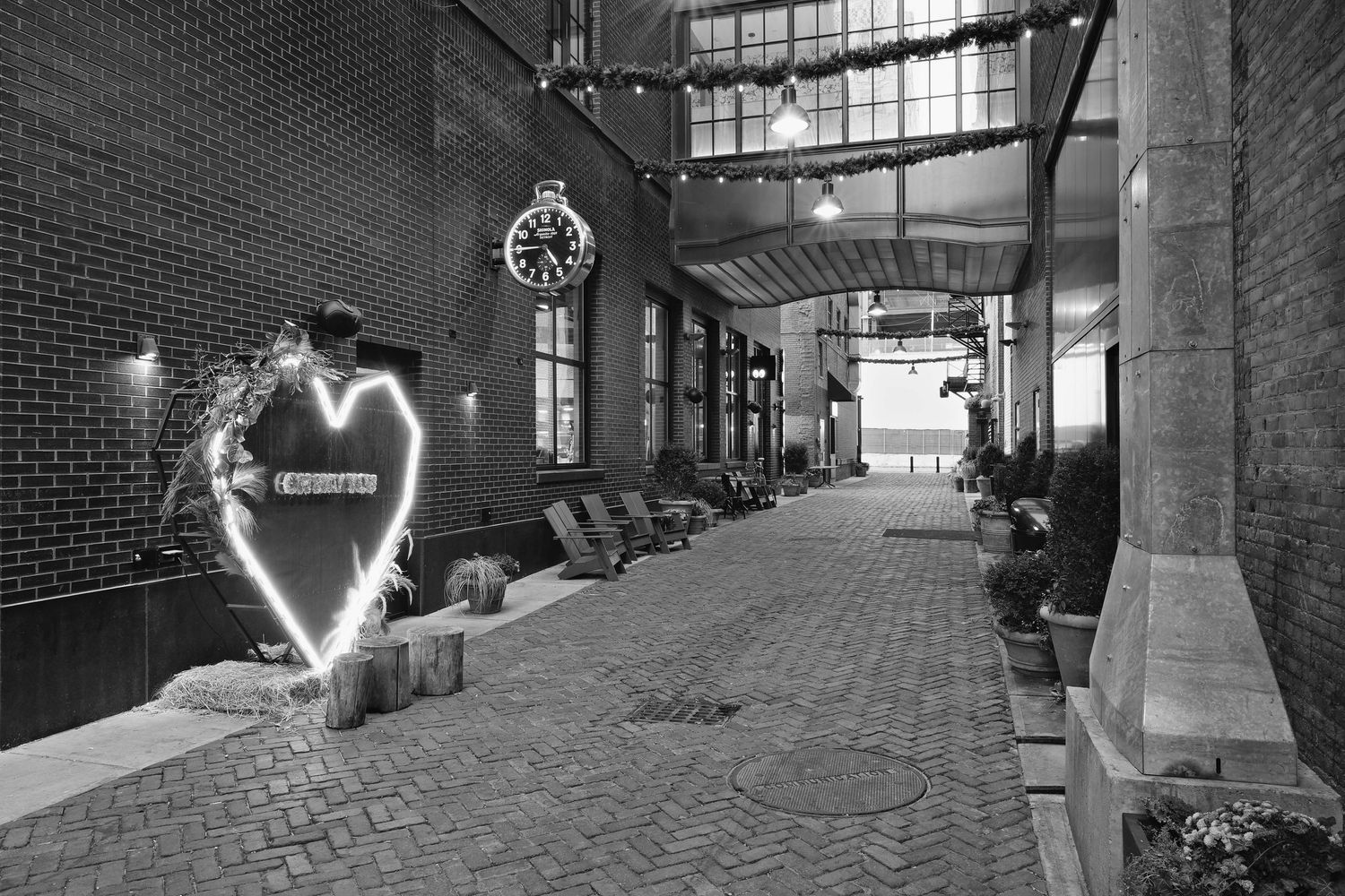 A black and white photograph of Parker's Alley in Detroit, Michigan with an illuminated heart and a Shinola clock on the brick wall.