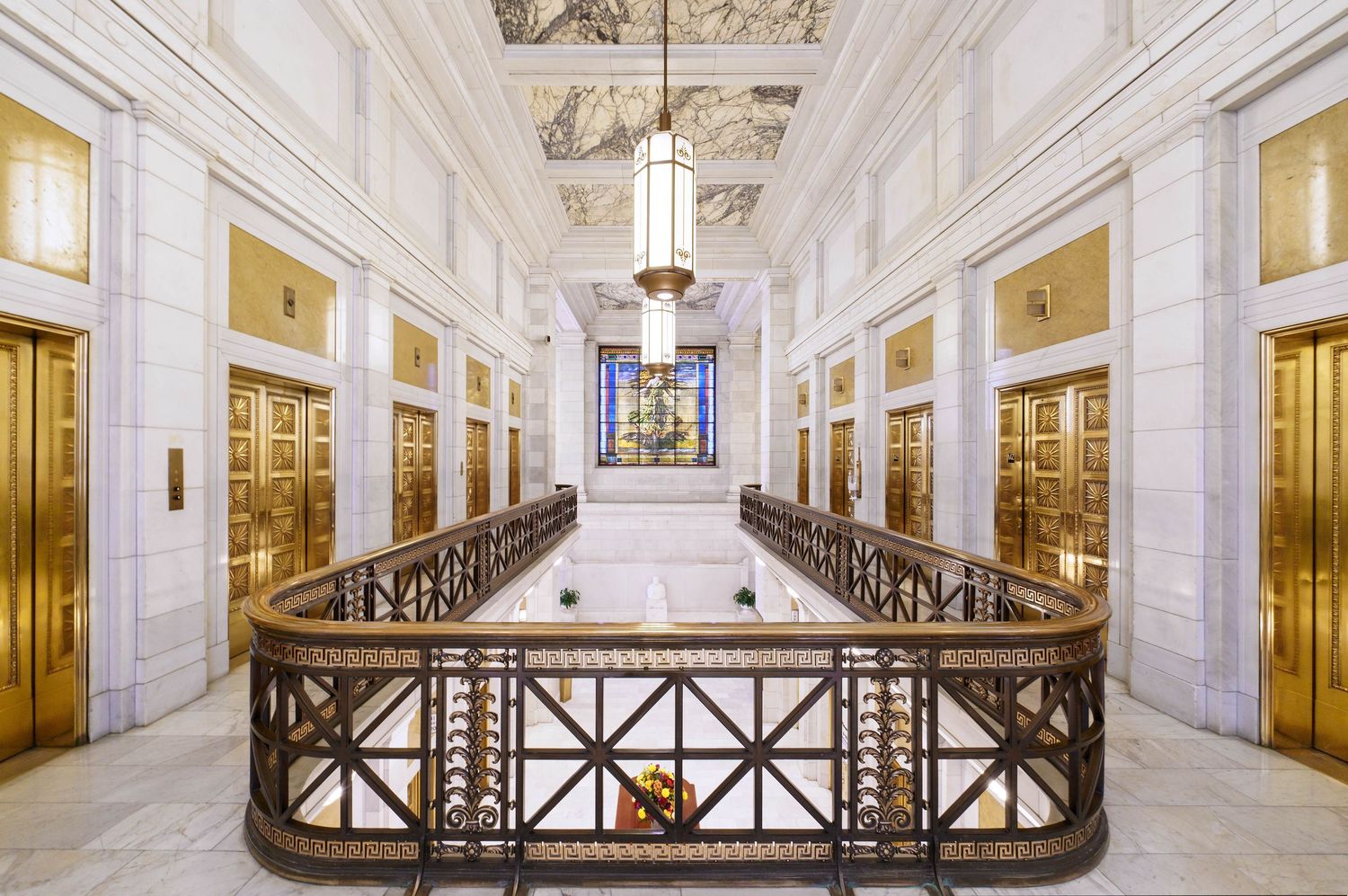 Ornate white marble interior of the Frick building in Pittsburgh with elegant architectural details and golden elevators and stained glass.