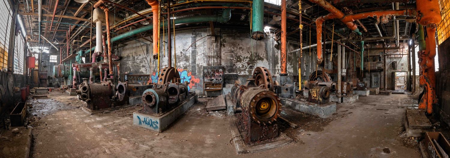 Panoramic view of an abandoned industrial warehouse interior with rusty machinery and equipment.