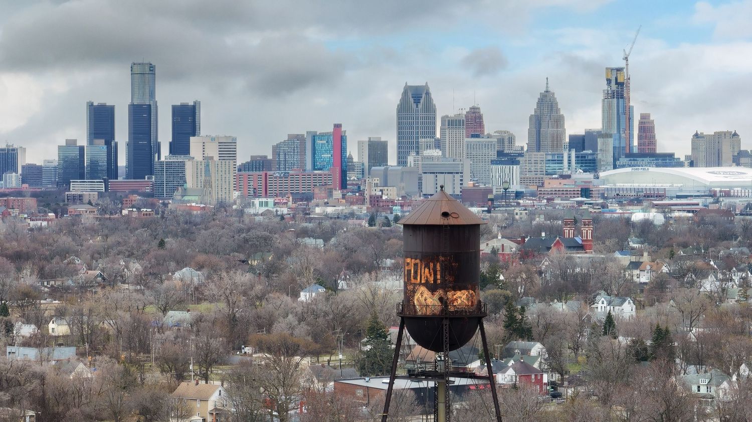 Panoramic cityscape view of Detroit skyline with water tower in the foreground and cloudy skies.