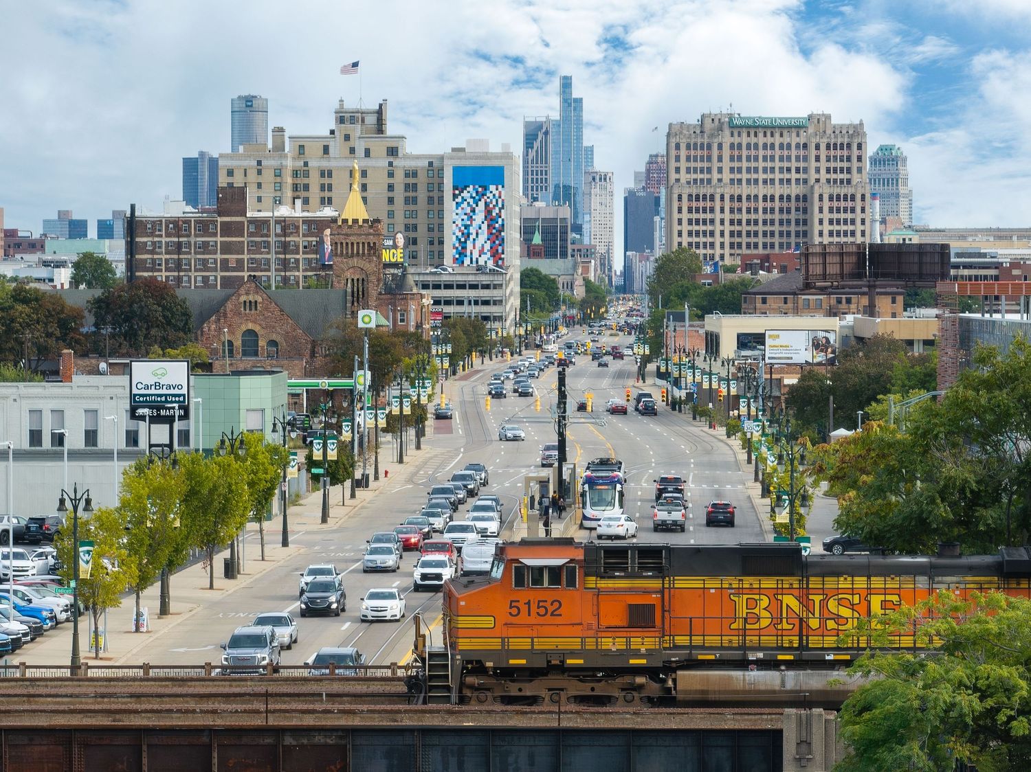 Aerial panoramic view of Detroit along Woodward Avenue on a sunny day with a locomotive in the foreground.
