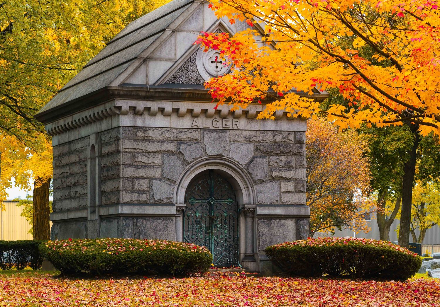 Historic Elmwood cemetery mausoleum under vibrant orange fall foliage in Detroit, MI.