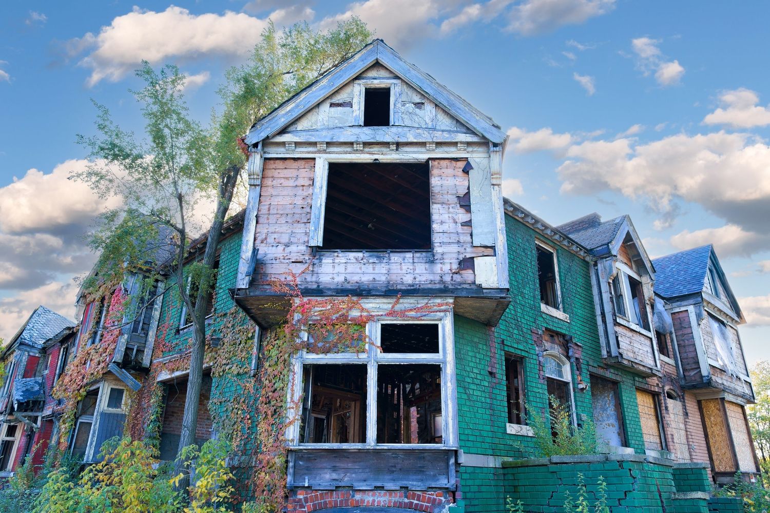 Row of abandoned houses with deteriorating roofs against a bright blue sky in Detroit, Michigan.