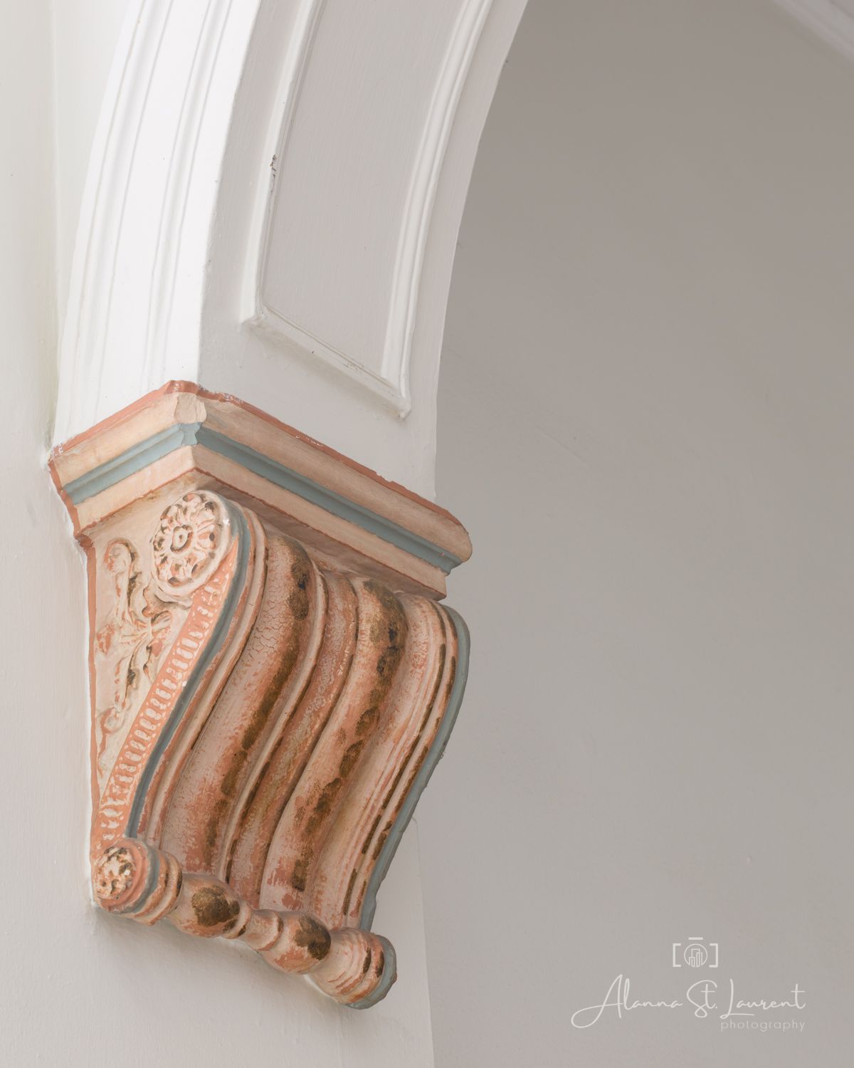 Ornate pink and green corbel bracket detail on a white arched architectural column in a classical building interior.