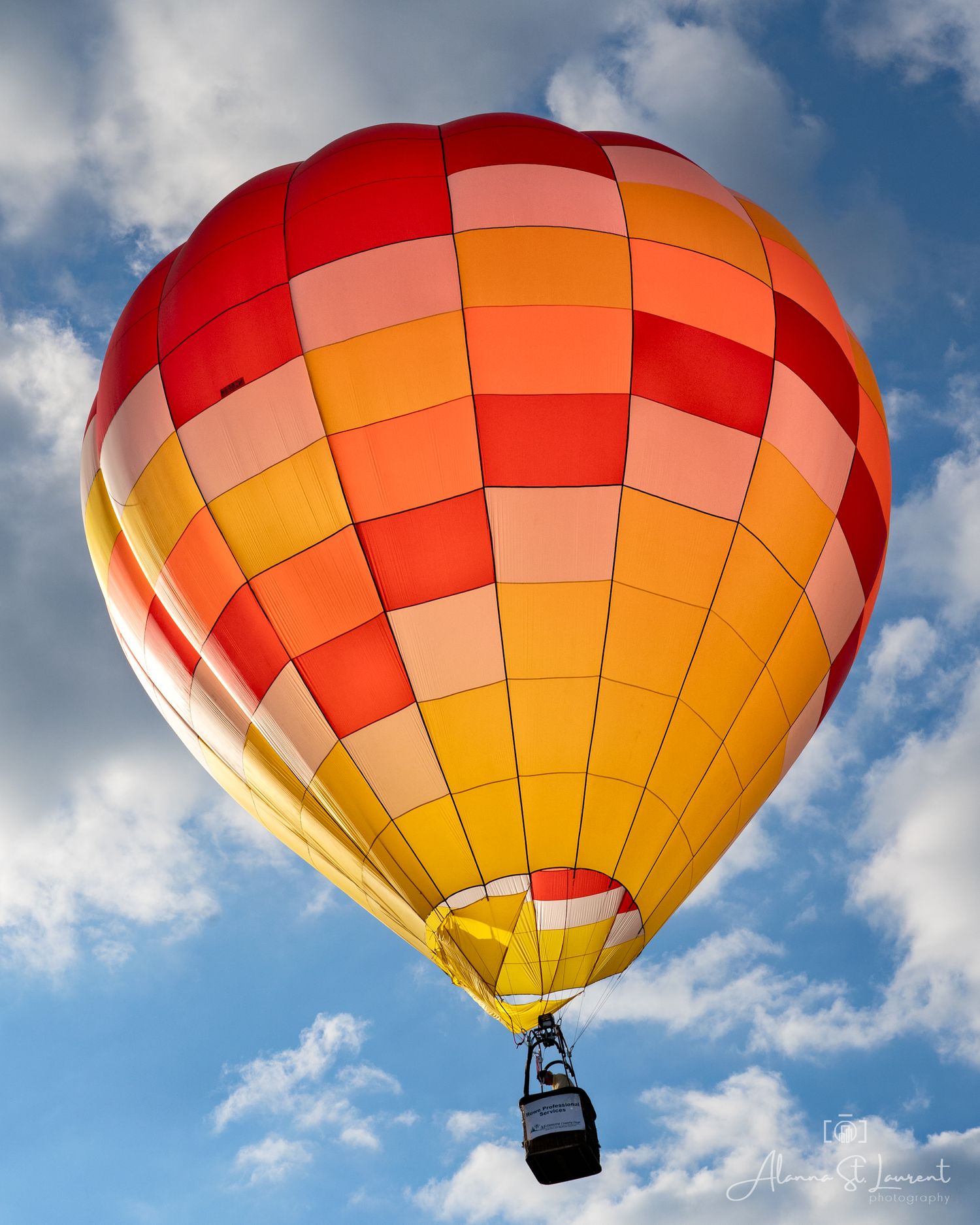 Red and yellow gradient hot air balloon floating in a partly cloudy blue sky in Metamora, Michigan.