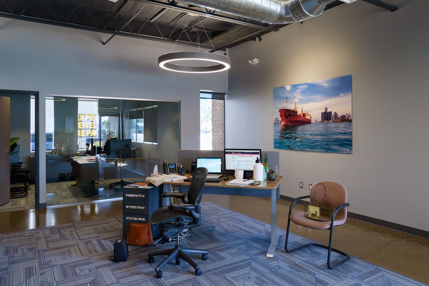 Contemporary workspace featuring minimalist furniture and industrial ceiling design with photo with a red freighter on the wall.