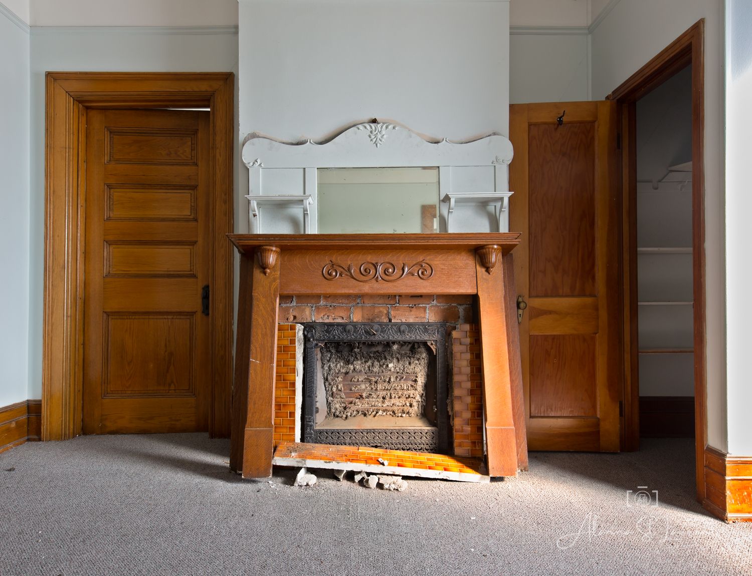Vintage wooden fireplace mantel with ornate mirror in an empty room with carpet and classic wooden doors.