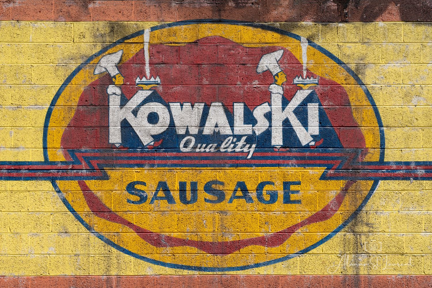 Vintage Kowalski Quality Sausage painted advertisement on a yellow and red brick wall.