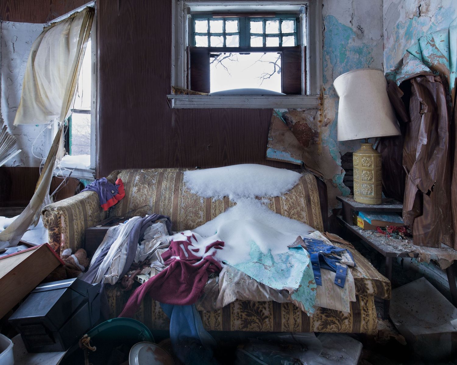 Deteriorating room interior with broken windows and damaged walls in a living room of an abandoned home in Detroit, Michigan.