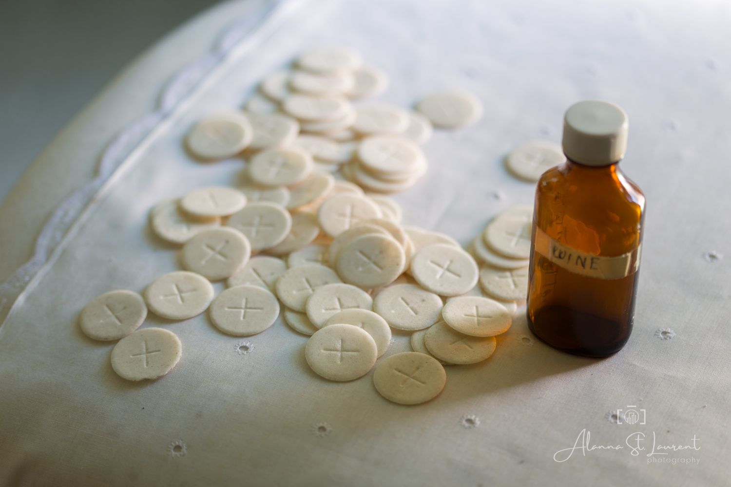 Communion wafers and a small amber glass bottle arranged on a white cloth surface.