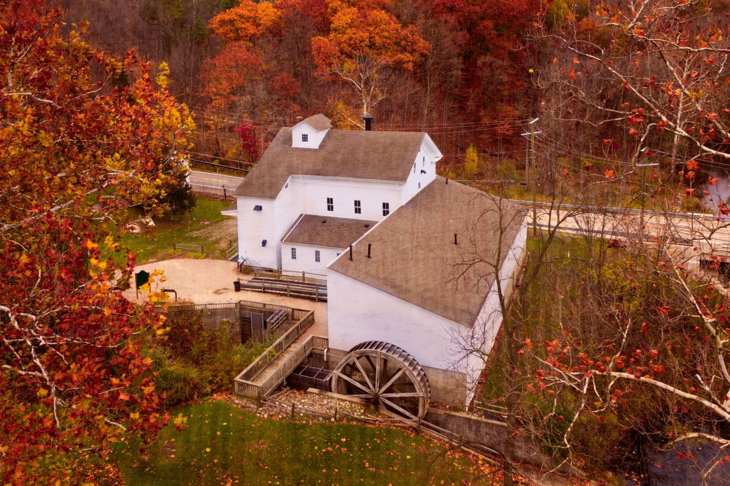 Aerial view of Wolcott Mills Park historic mill with water wheel nestled among fall foliage with painterly texture.