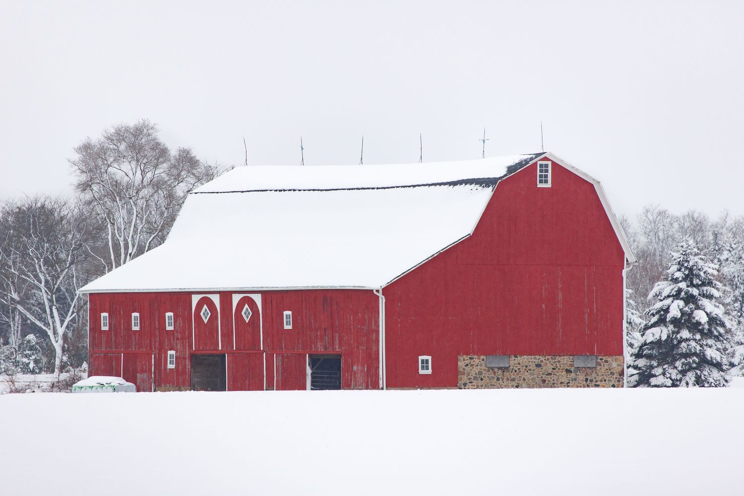 Classic red barn with white roofs nestled in a snow-covered countryside near Manchester, Michigan.