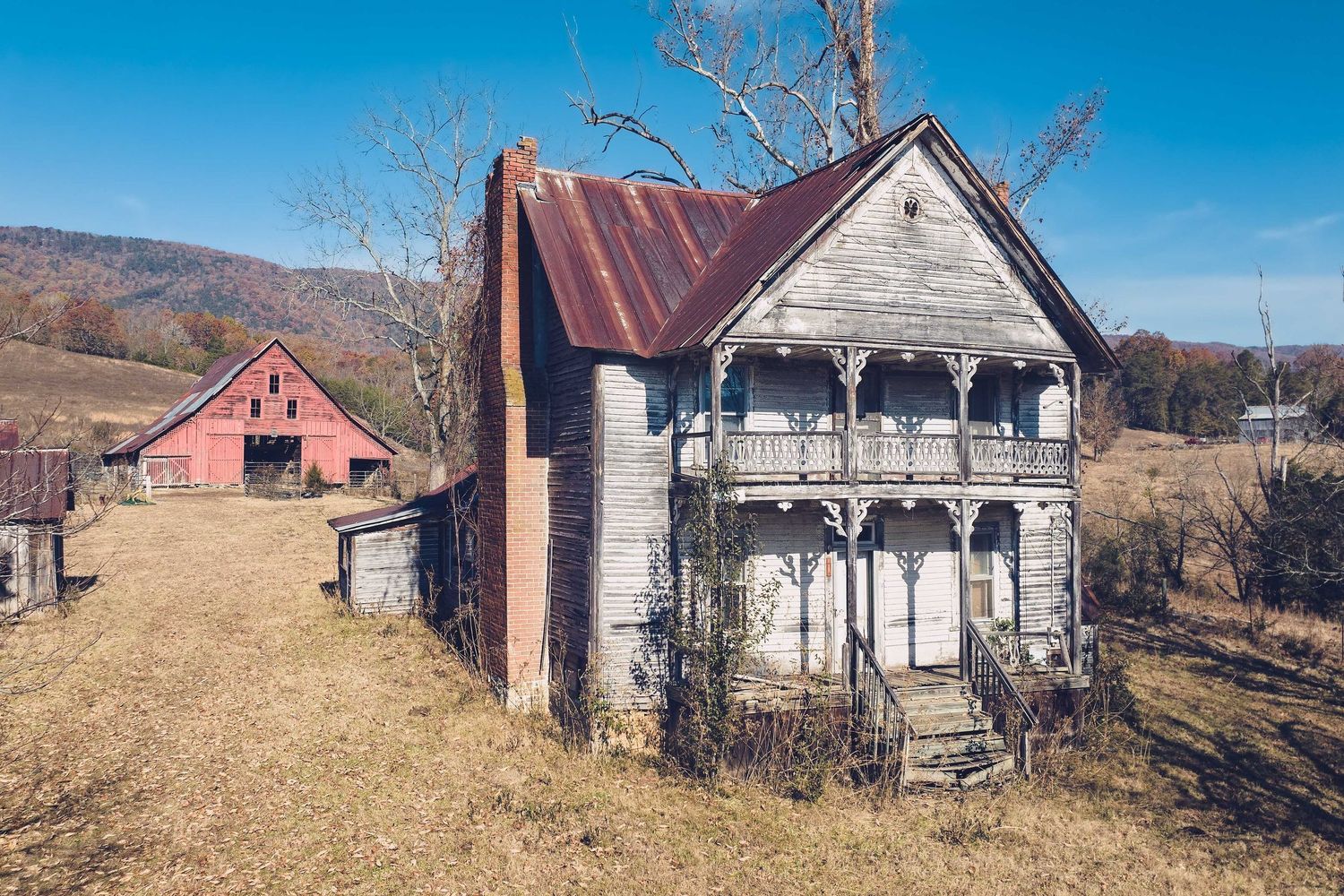 An abandoned rural farmhouse and barn in outside Rutledge Tennessee against a blue sky.