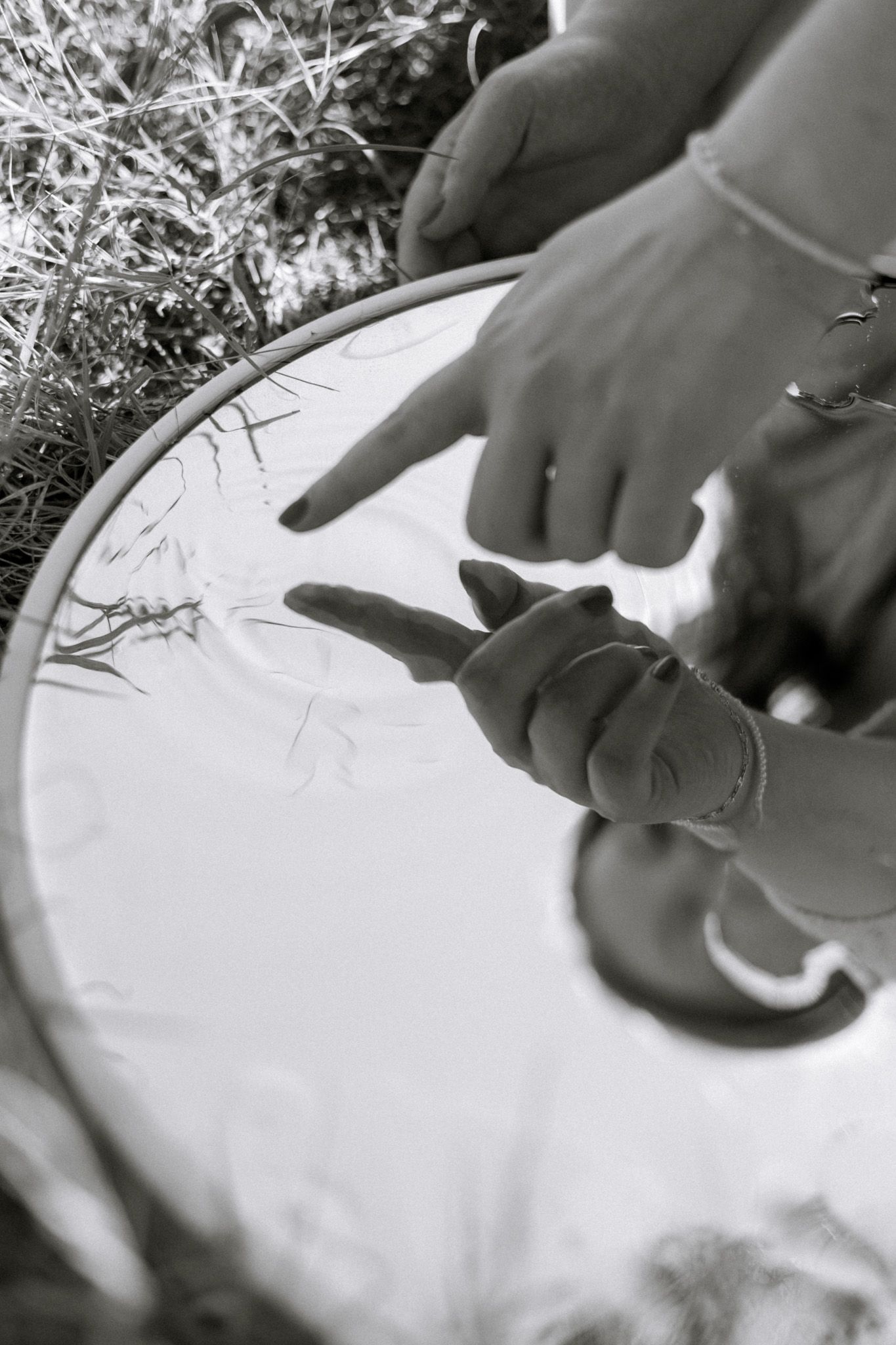A young adult girl is touching a mirror with water. The water on the mirror gives off a ripple effect. The image is in black and white.