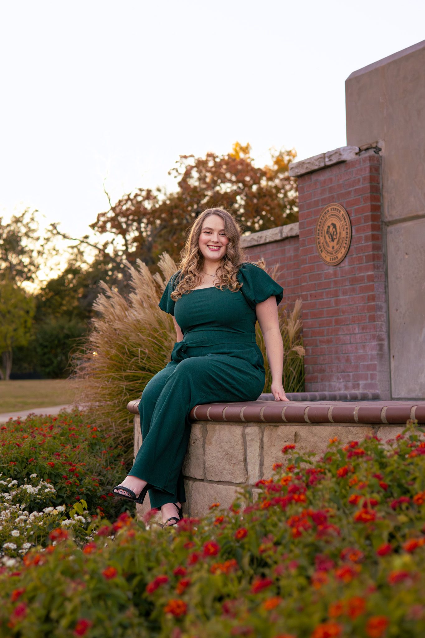 A young adult girl is smiling and is sitting on a fountain.