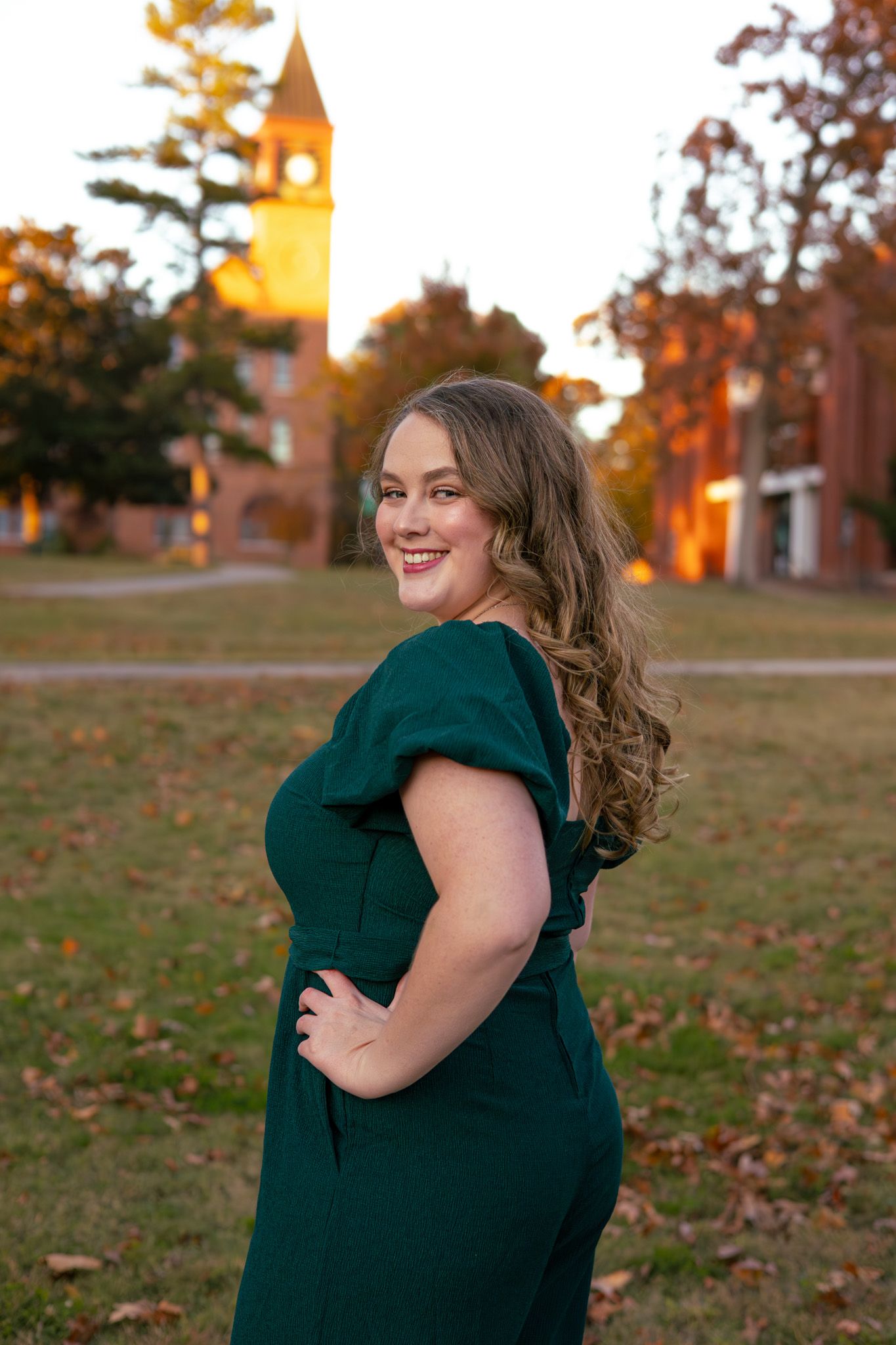 A young adult girl in front of her historic college building. She has a hand on her hip and is smiling.