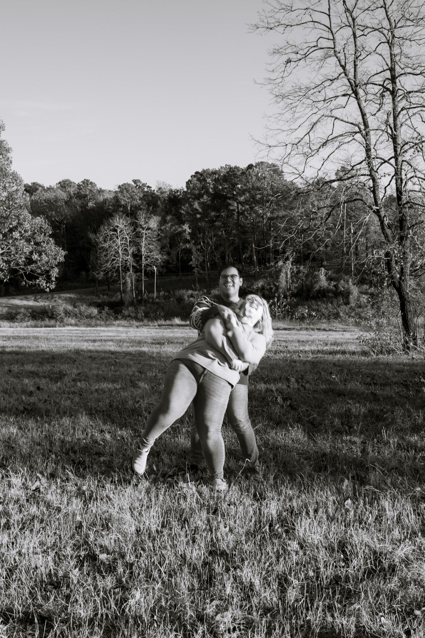 A young adult couple dancing and holding eachother close while laughing. The image is blurry for a dreamy effect and is black and white.