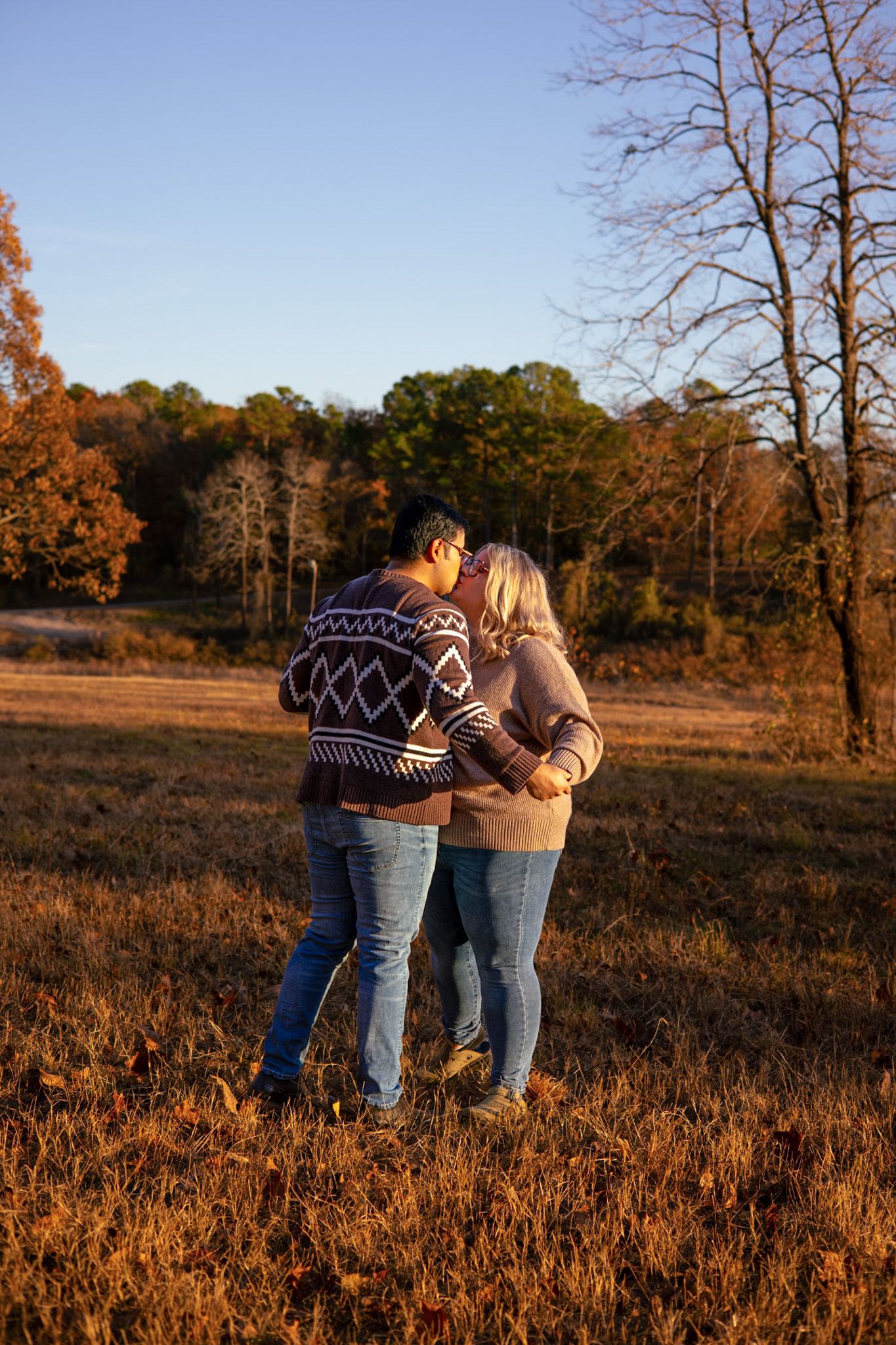 A young adult couple kissing in a field. The color of the image is very orange because of the fall scenery.