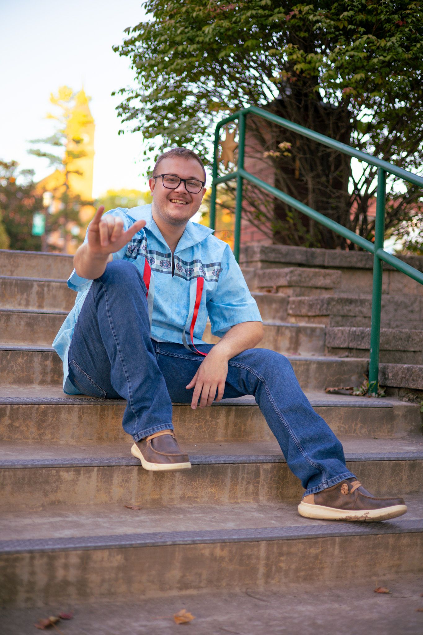 A young adult boy is sitting on stairs and is holding up his university hand sign 