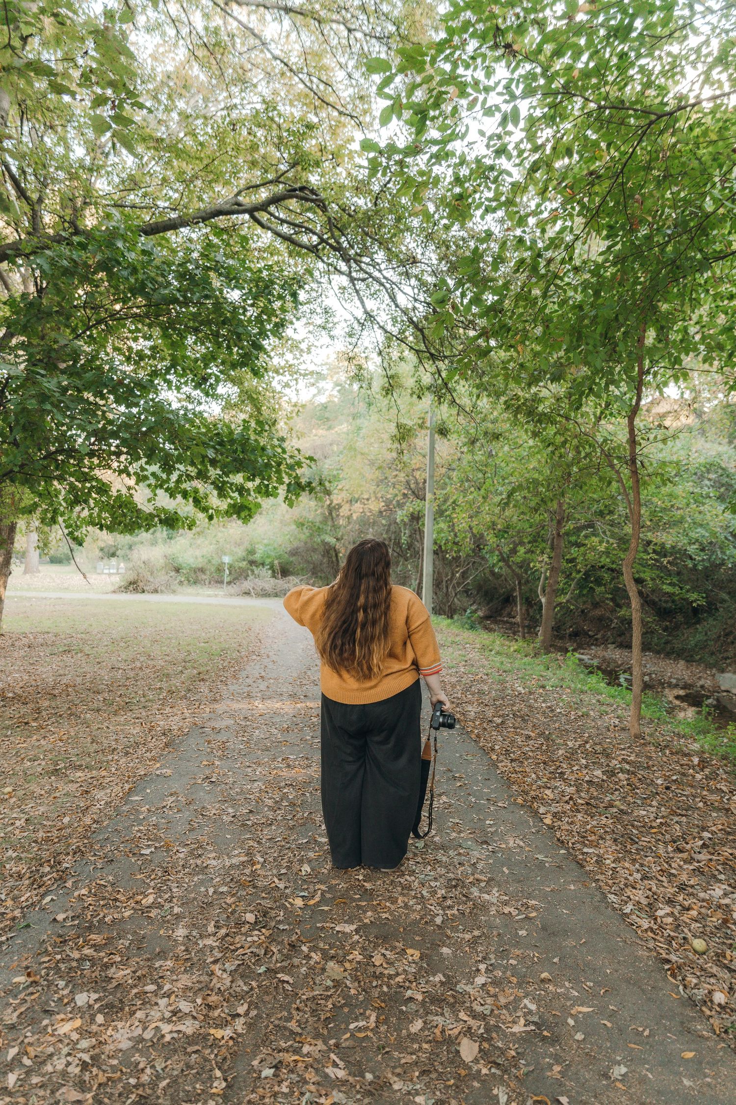 A young adult girl walking with her camera at her side. She is looking away from the camera for a dramatic photo effect.