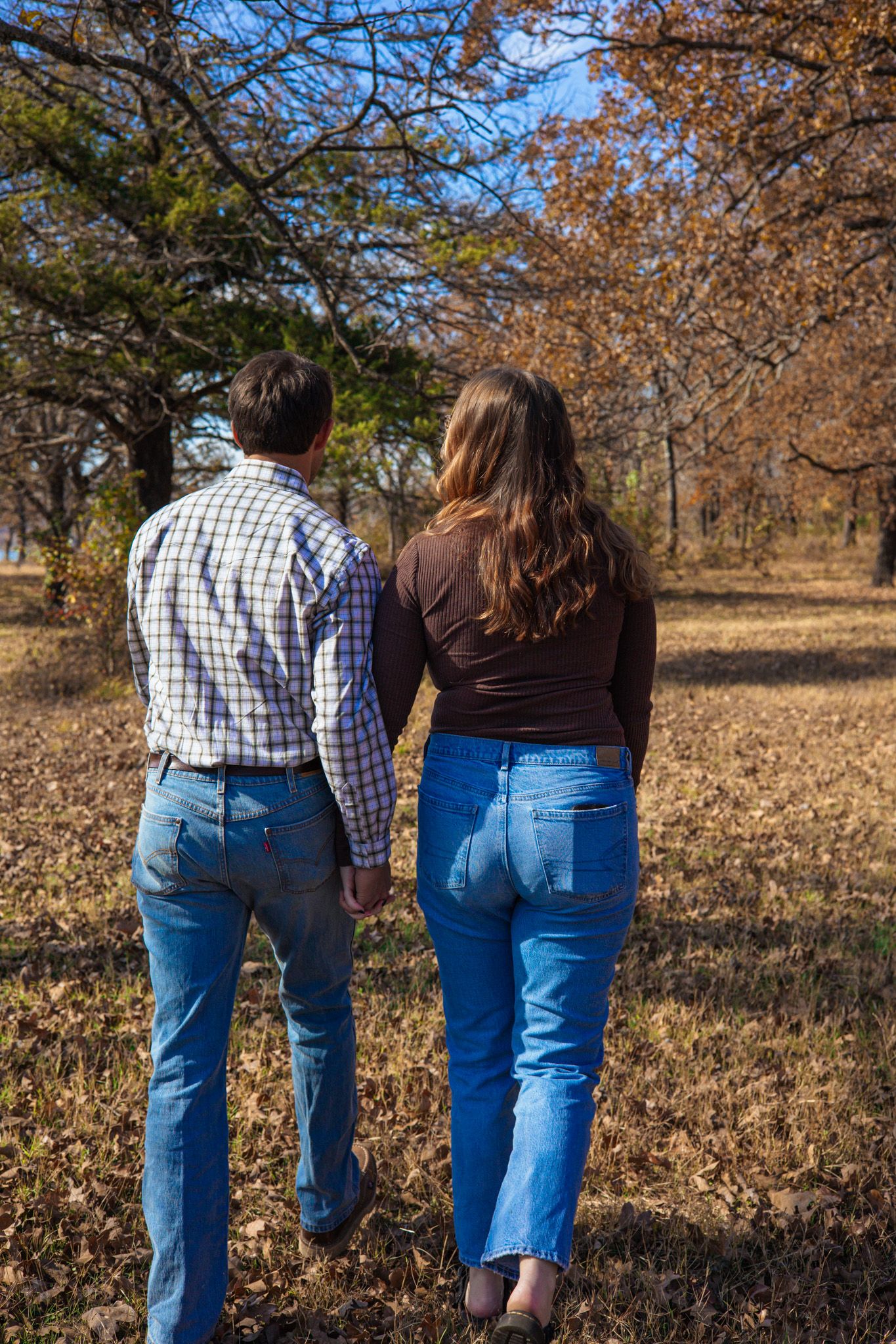 A young adult couple holding hands and walking away from the camera.