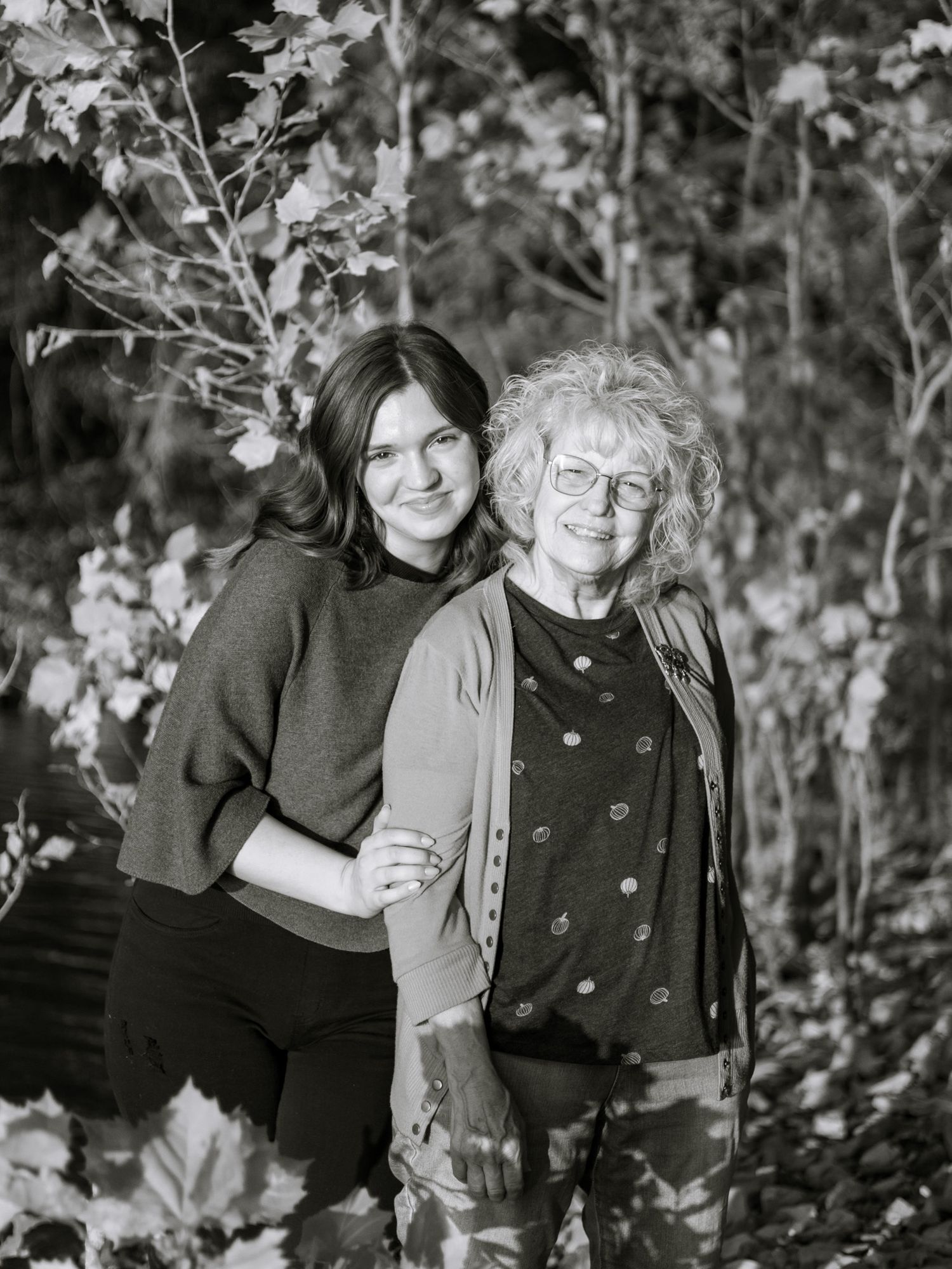 A young adult girl and her grandma are holding each other close and facing the camera with big smiles. The image is in black and white.