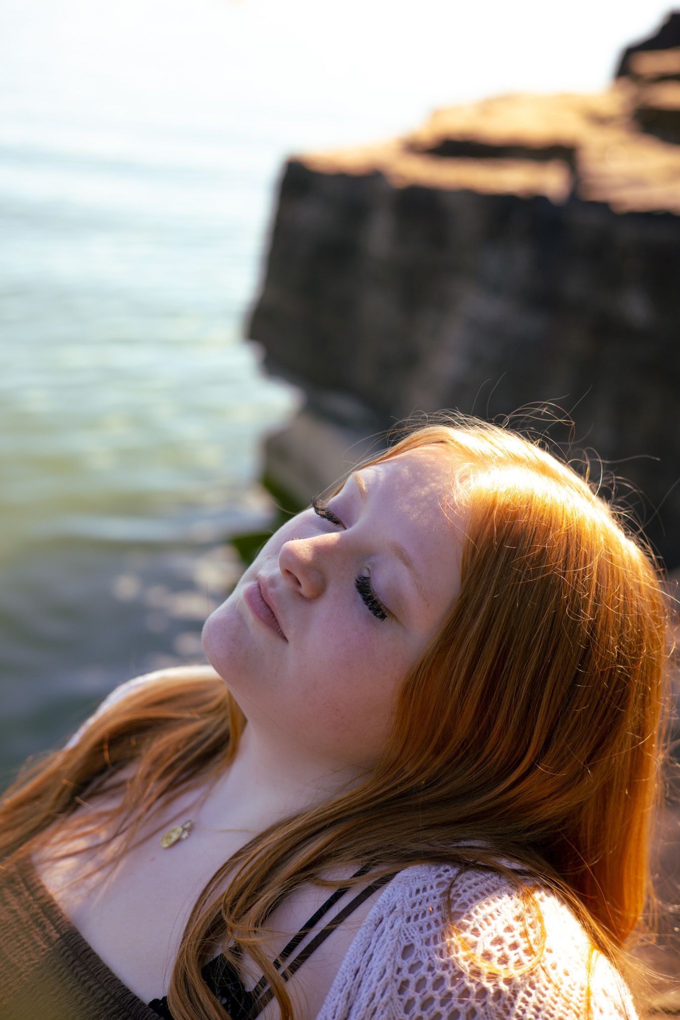 A young adult girl with her head back and her eyes closed. She is pictured as resting or soaking in the sun.