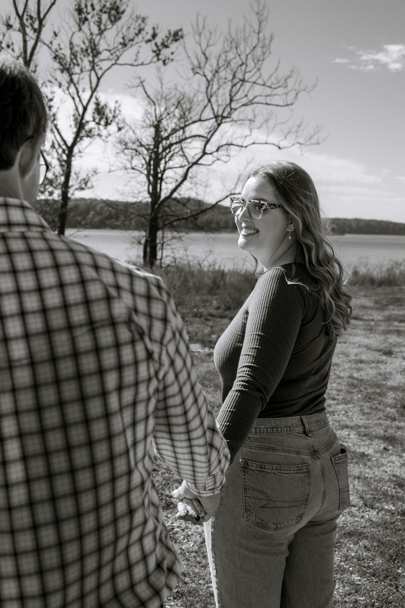A young adult couple faces away from the camera and looks at each other holding hands. The image is in black and white.