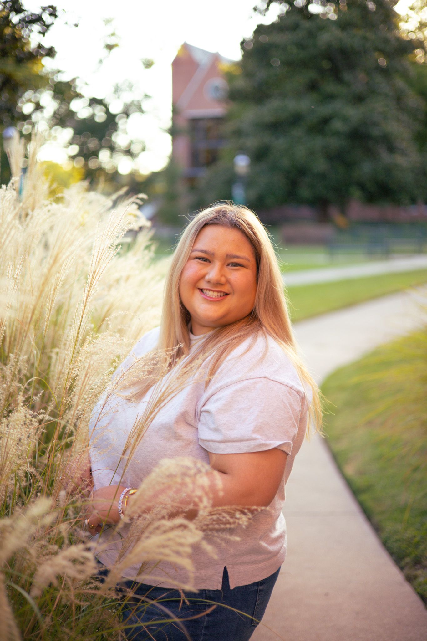 A young adult girl is smiling at the camera in front of a bush.