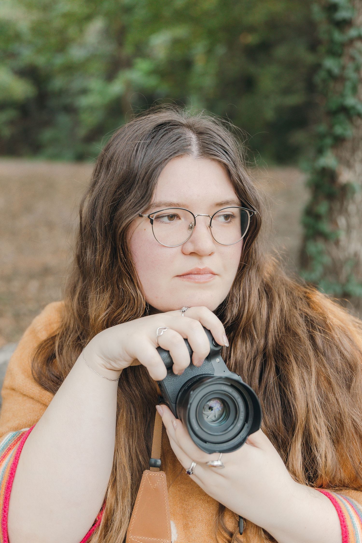 A young adult girl holding a camera and is looking off in the distance.