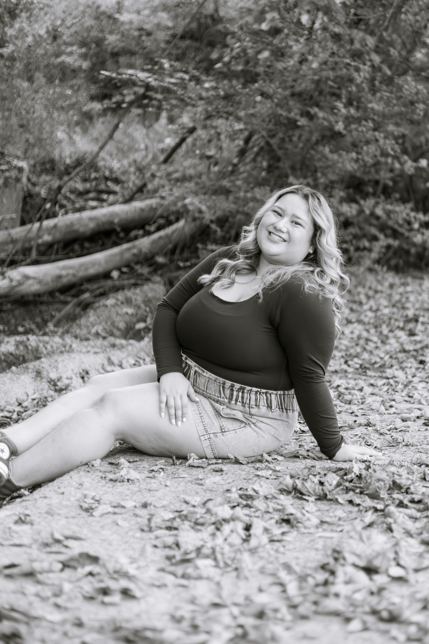 A young adult girl is sitting on the ground with an arm propping her up. She is smiling, and the image is in black and white.