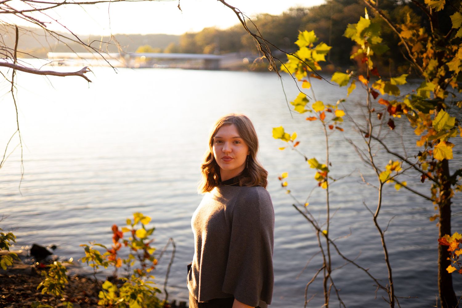 A young adult girl standing in front of a lake. Her face is black for a dramatic photo effect.