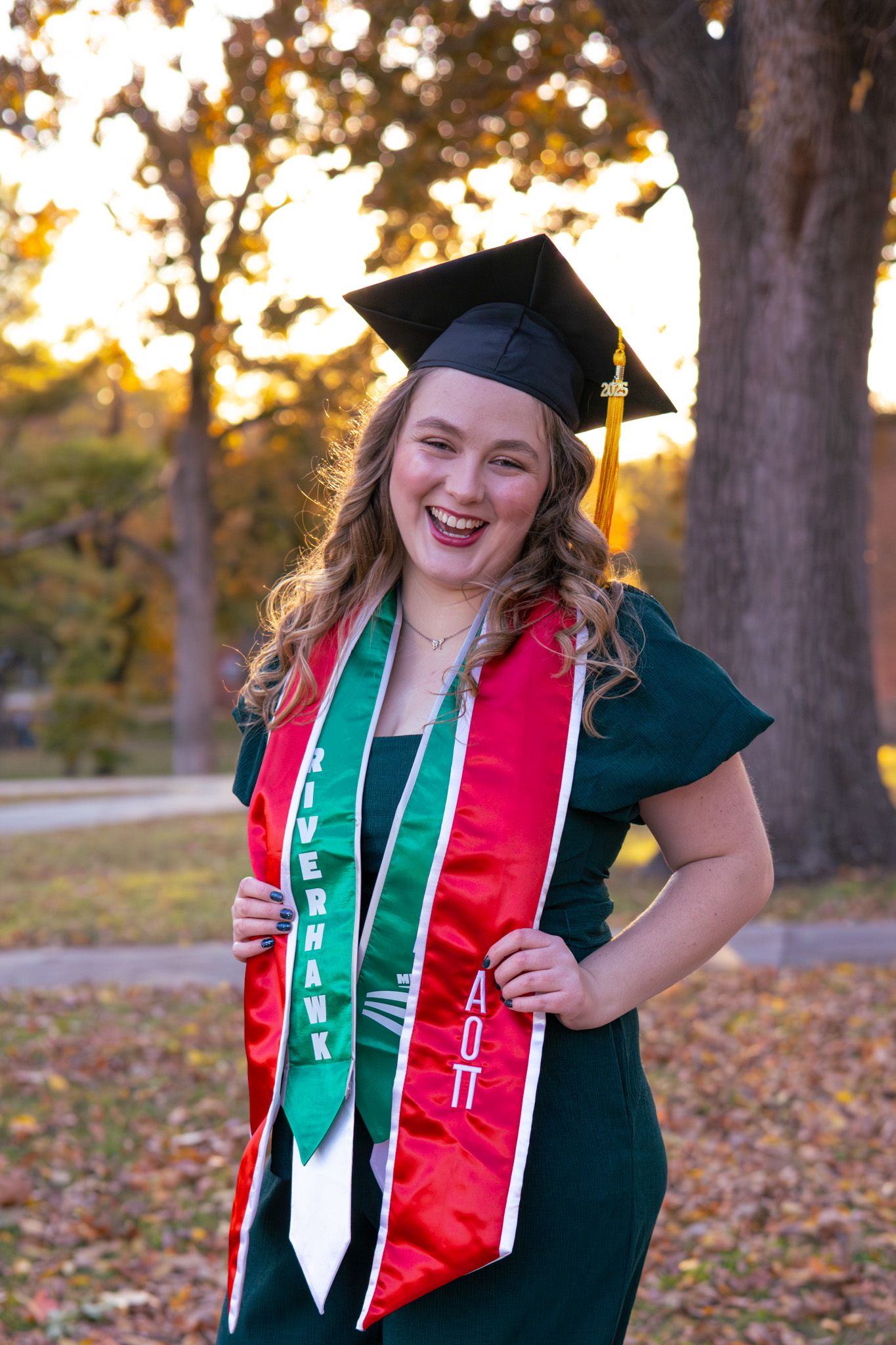 A young adult girl wearing graduation regalia and is smiling for the camera.
