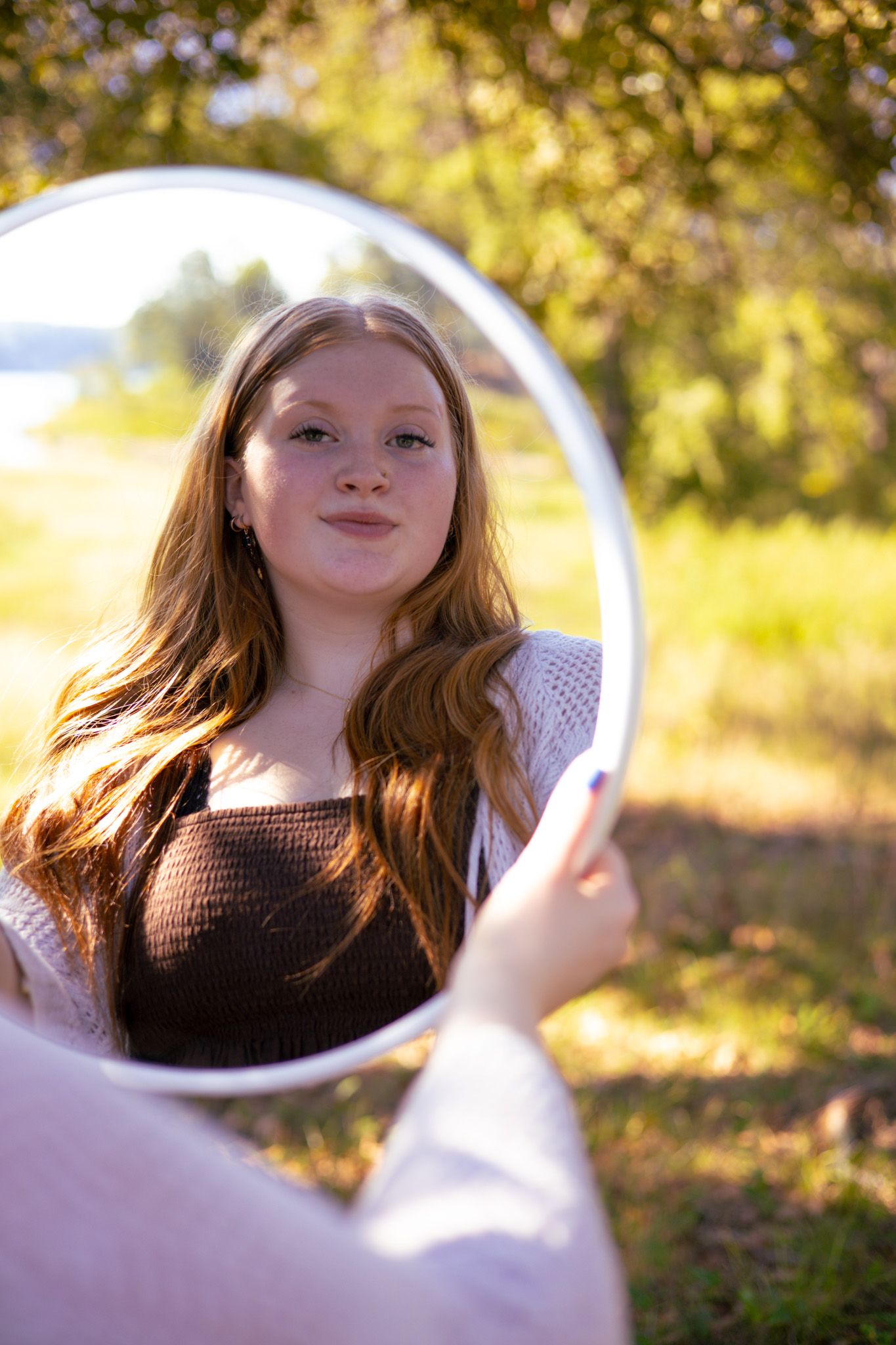 A young adult girl holding a mirror and looking in it.