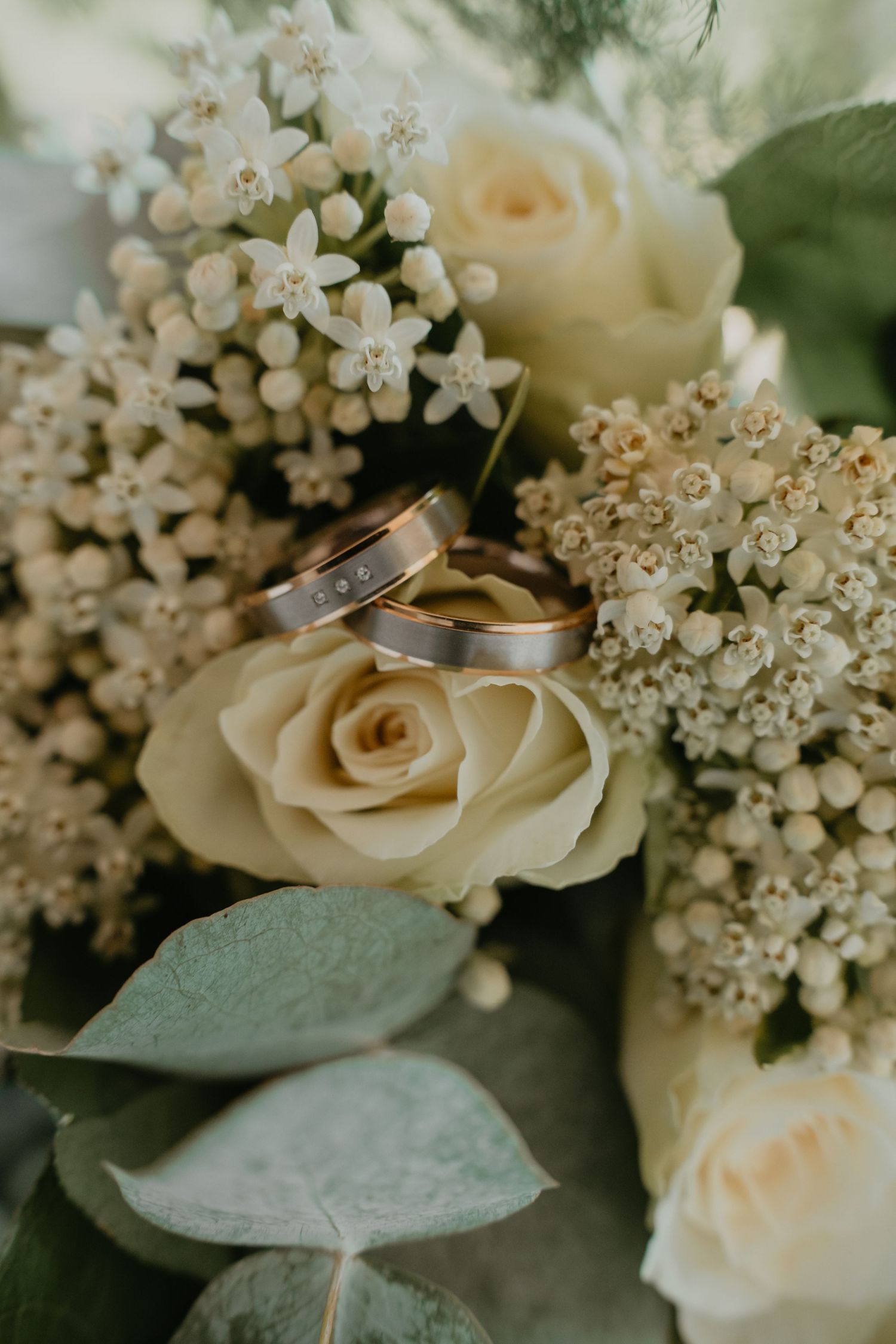 Bruidsboeket met witte bloemen, groene details en de trouwringen van het bruidspaar