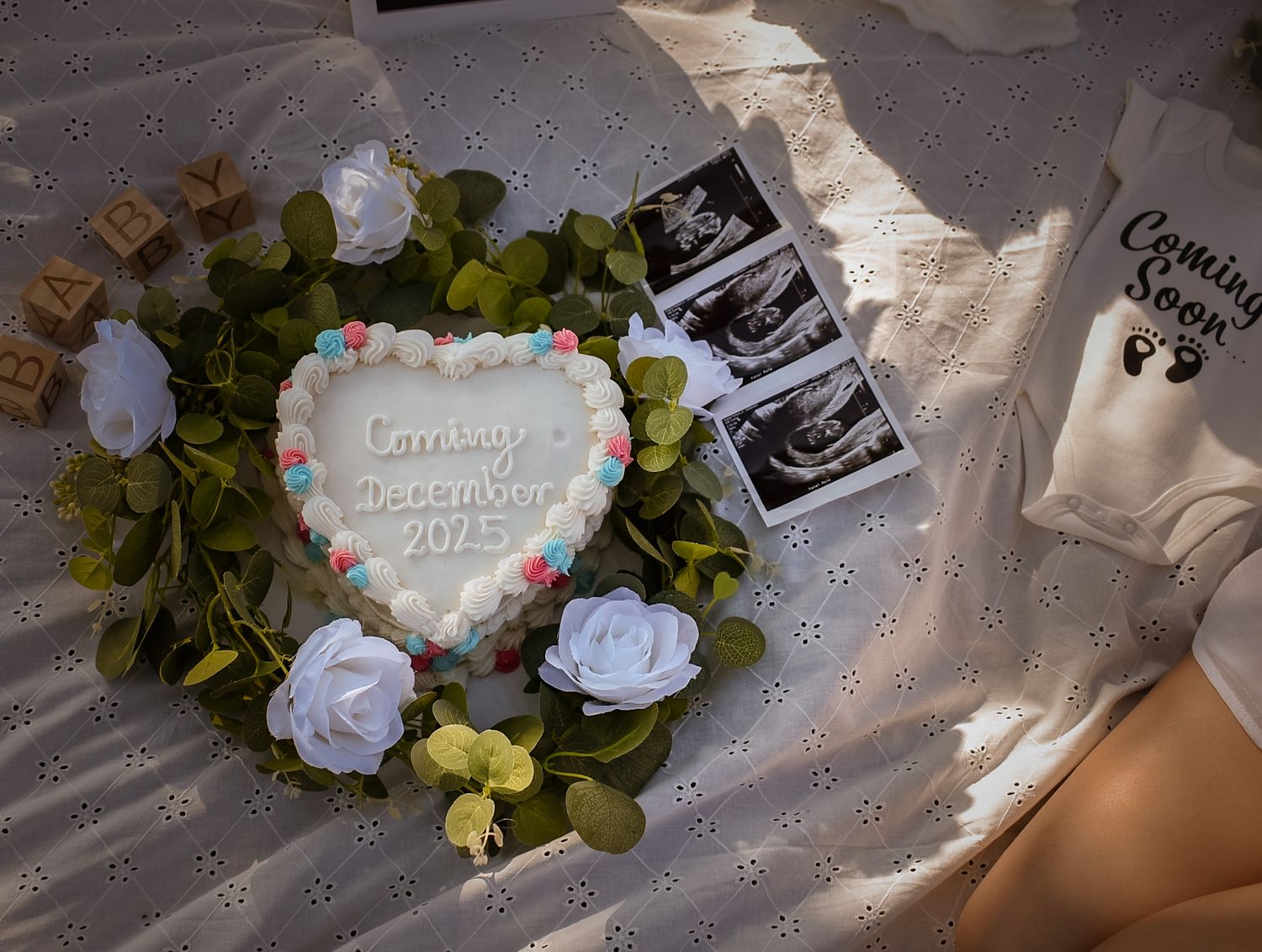 Heart-shaped baby shower cake surrounded by white roses and ultrasound photos on a decorated table.