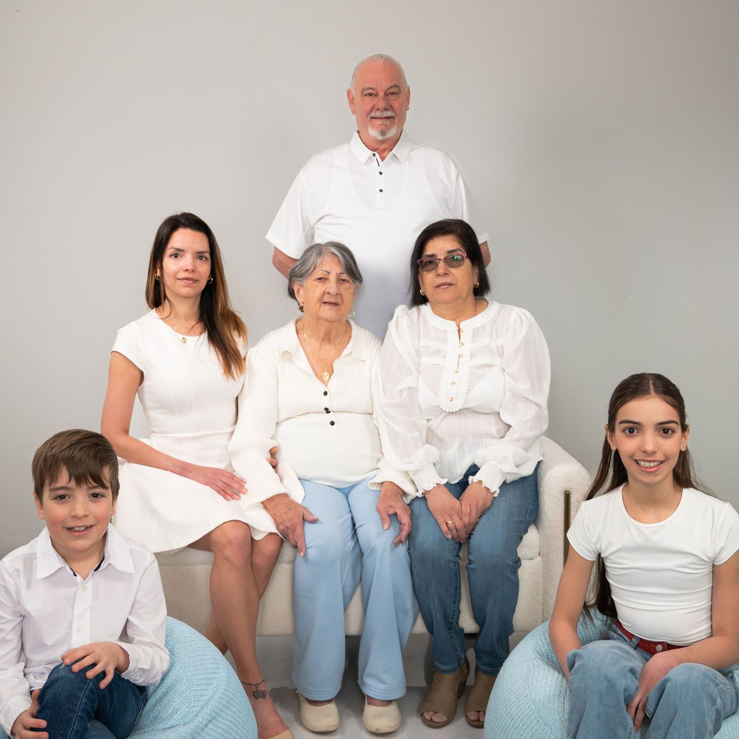 Multi-generational family of six poses together in matching white outfits for a formal portrait photo.