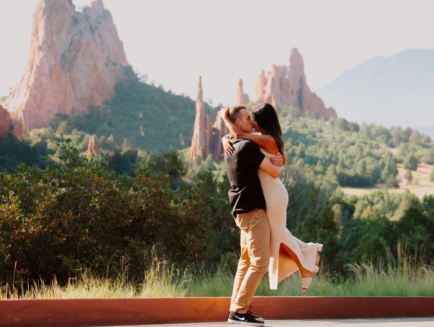 Couple sharing romantic kiss at Garden of the Gods park with red rock formations backdrop.