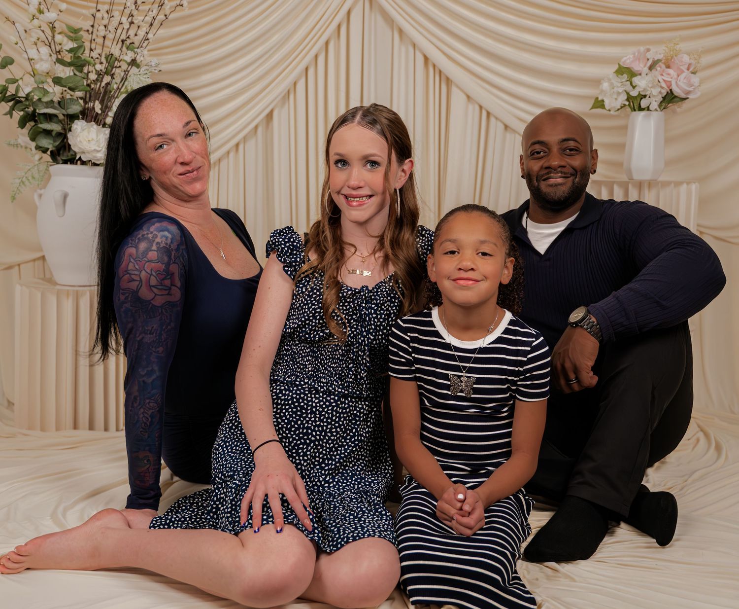 Family of four posing together for a portrait in a elegant white draped studio setting.