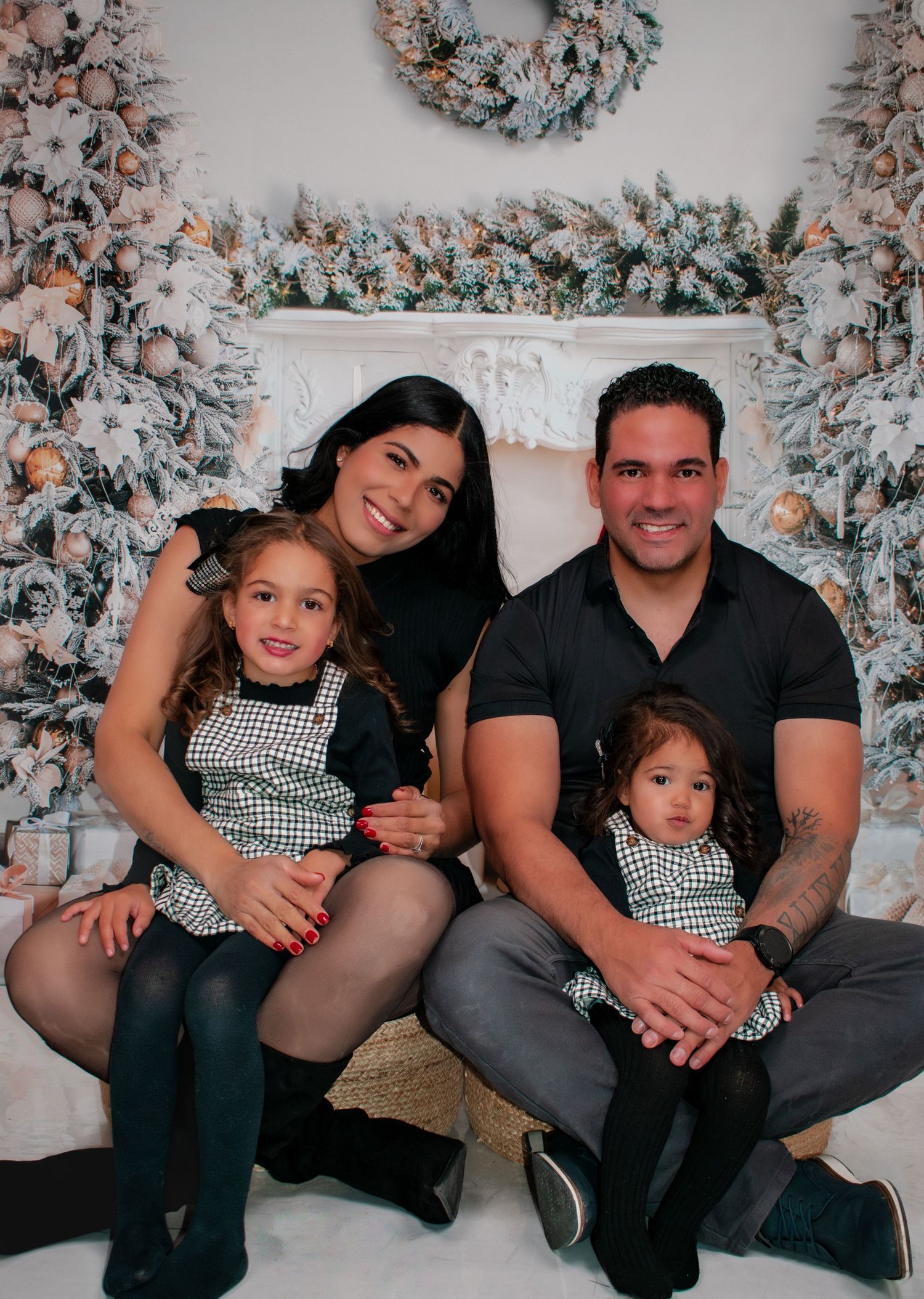 Family of four in matching black checkered outfits posing in front of white flocked Christmas trees.