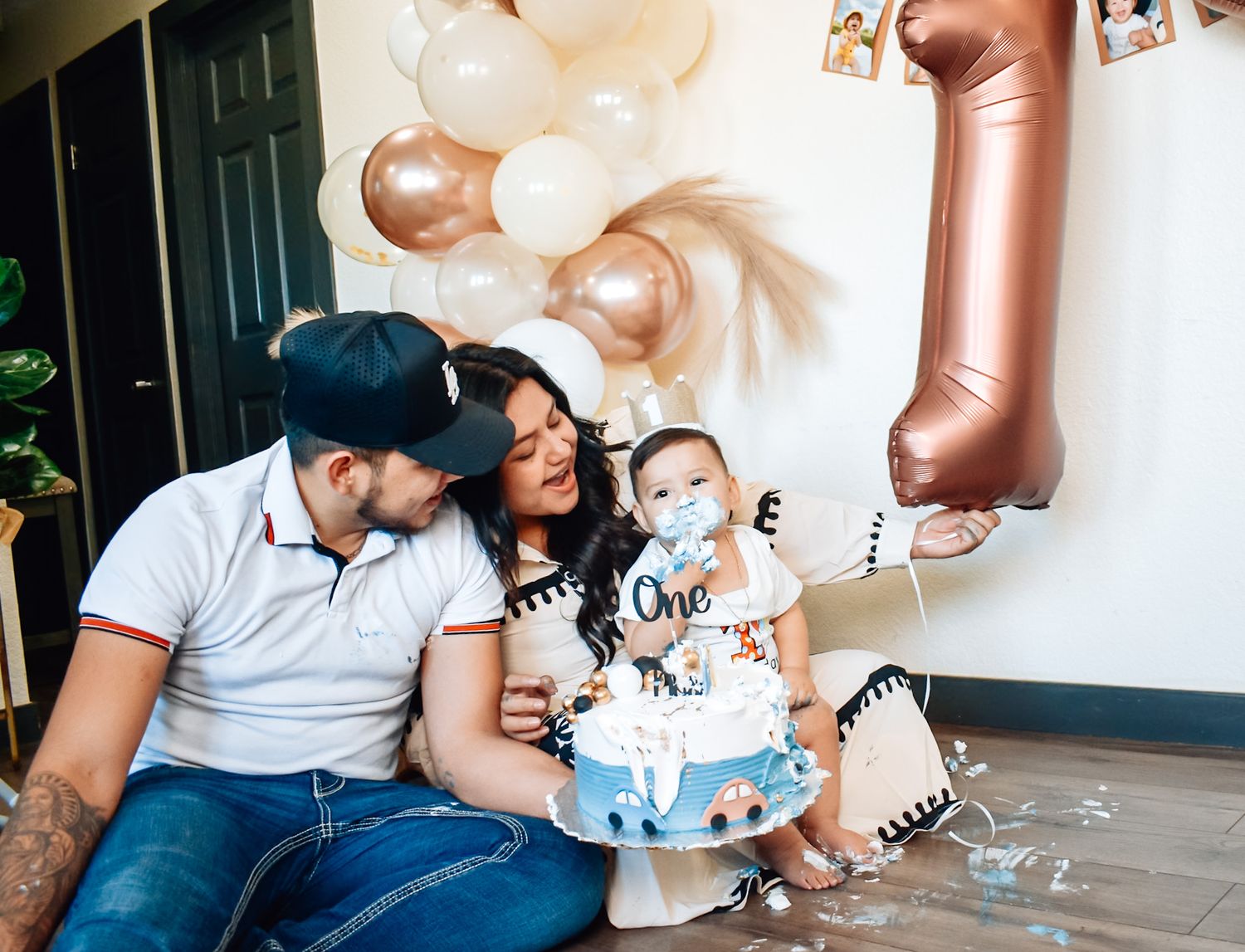 A couple celebrates their baby's first birthday with a decorated cake and balloon decorations.