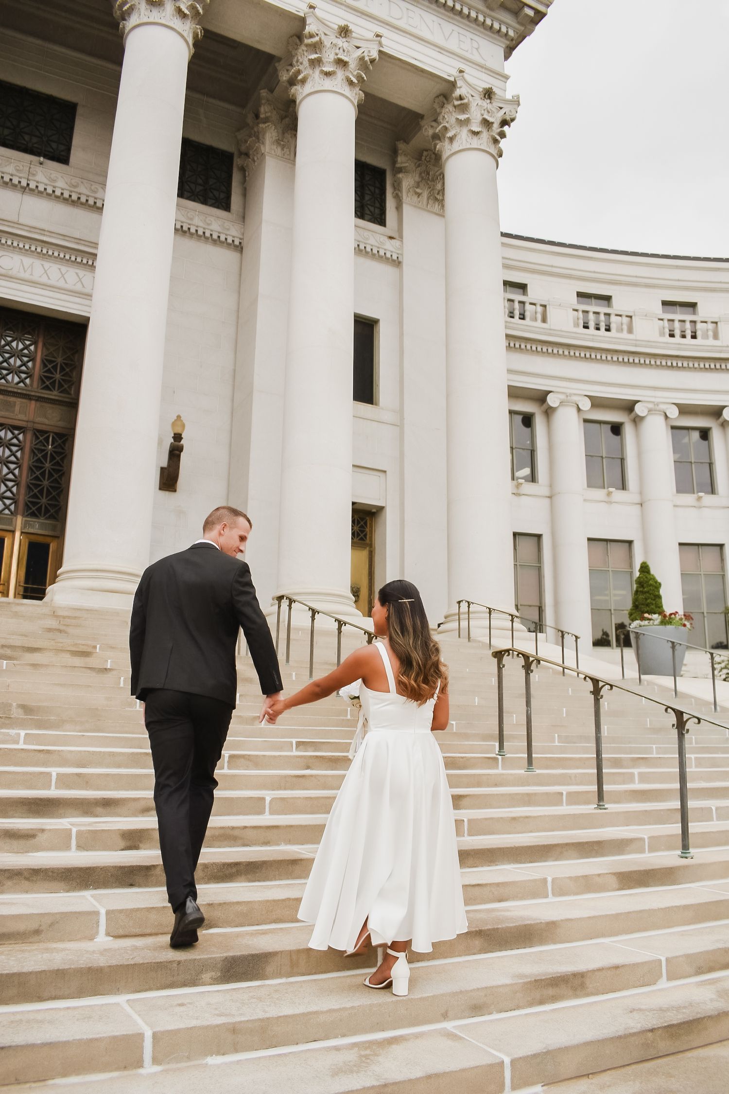 Bride and groom holding hands walking up steps of elegant white columned building.