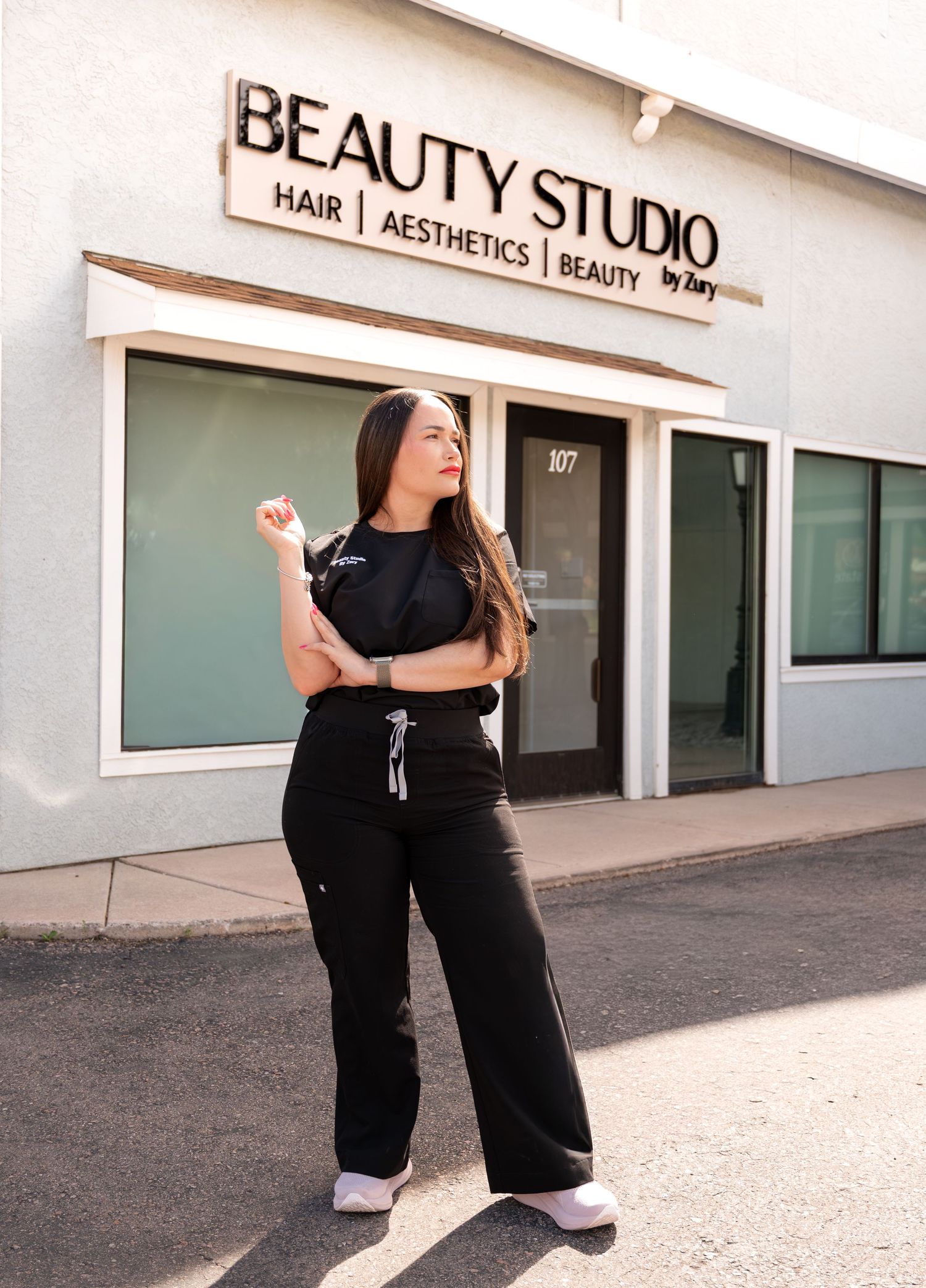 Woman in black scrubs poses outside Beauty Studio by Zary, offering hair, aesthetics, and beauty services.